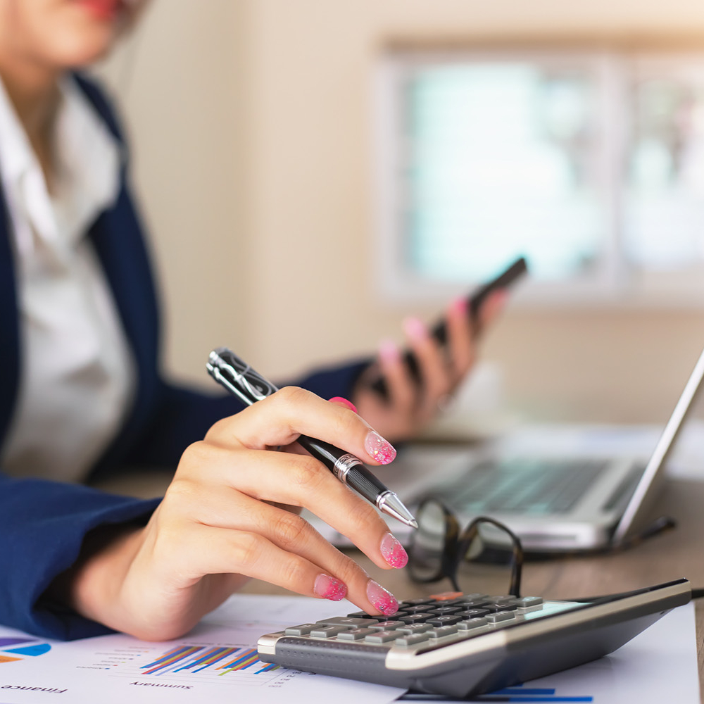 Woman with painted fingernails using calculator while working in finance.