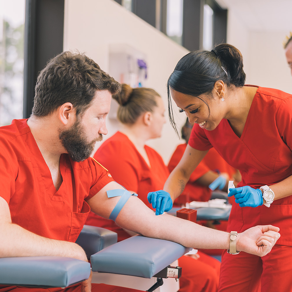 African American woman practices a blood draw on her caucasian male classmate with class.