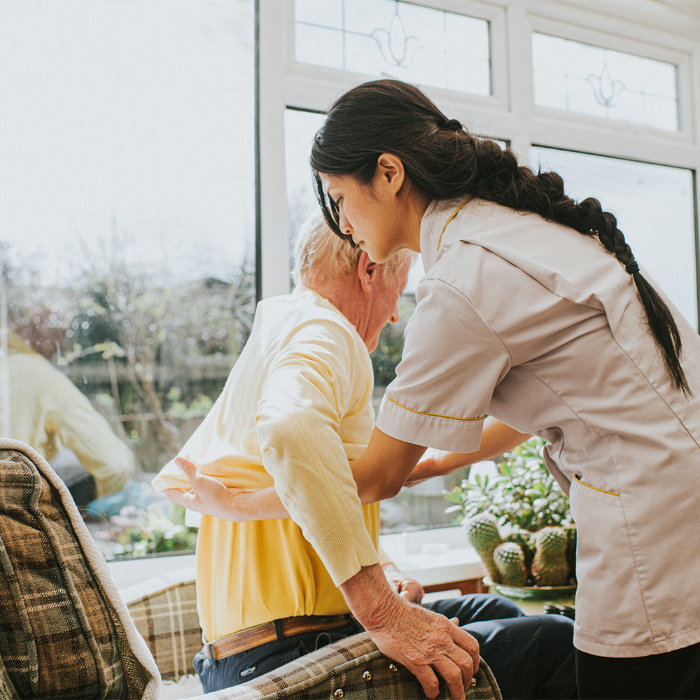 In home nurse helping elderly man up from his chair by a window