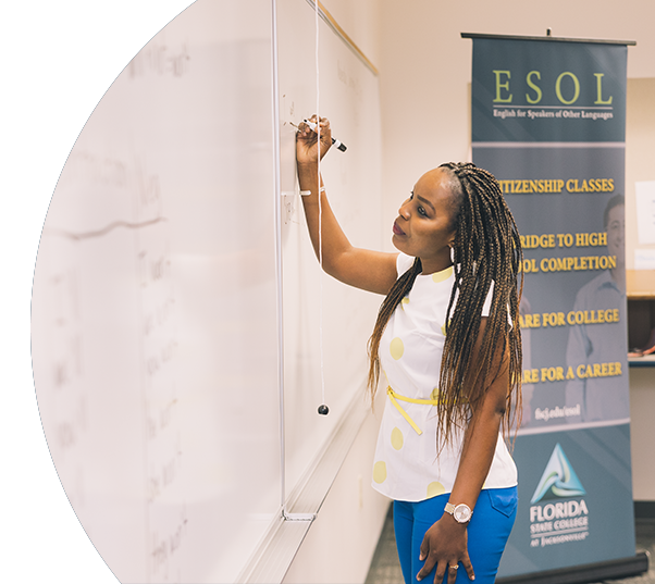 African American woman demonstrates her understanding of ESOL class in Adult Education on a whiteboard in front of the class.